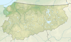 Mapa konturowa województwa warmińsko-mazurskiego, u góry po prawej znajduje się owalna plamka nieco zaostrzona i wystająca na lewo w swoim dolnym rogu z opisem „Łaźno”