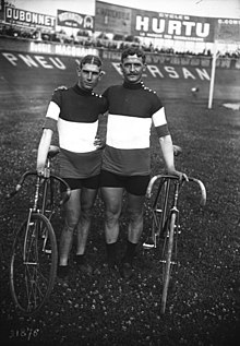 Photographie noir et blanc de deux cyclistes à l'arrêt avec leurs machines.