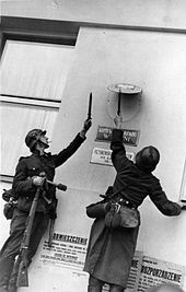 Photo of two German soldiers removing Polish government insignia from a wall.