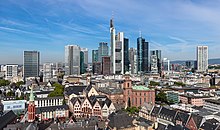 Quartier d'immeubles avec des habitations, des religions, un peu d'arbres, et plus loin devant le ciel de nombreuses pointes.