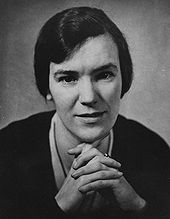 A black-and-white photograph of a middle-aged woman facing the camera. She had dark black hair and has her hands clasped. She is wearing a plain necklace and earrings.