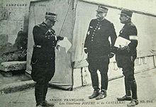 Photographie noir et blanc de trois hommes en uniforme, un lisant un document et un autre tenant un dossier dans la main.