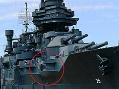 A permanently docked museum ship with a red circle on the photograph to highlight a gun protruding from an opening in the ship's port side.