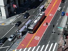 Overhead view of an urban arterial with red center lanes and a bus platform, with a bus at the platform