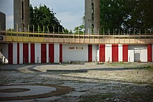 The abandoned interior of the Tent of Tomorrow as seen in 2018. There are weeds on the floor. The rear wall has a red-and-white striped wall with a sign advertising a skate rental.