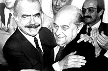 Sarney e Tancredo se abraçam, ao redor de outros políticos que os aplaudem.