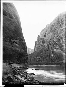 A boat floats on a river at the bottom of a rocky canyon