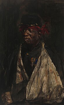 Portrait d'un soldat noir avec un bras en écharpe et un bandana rouge autour du front. Il porte deux médailles sur son uniforme militaire.