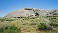 alt=Photograph of Independence Rock with sage-steppe vegetation in the foreground and the rock rising high abainst a clear sky.