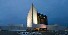 The John F. Kennedy Library, a white triangular tower, rises beside a black glass building, with circular structures on either side.