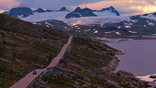 Voiture sur une route le long d'un lac avec un vaste glacier en arrière-plan.