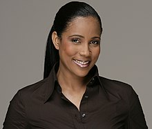 Photo portrait d'une femme noire aux cheveux longs qui porte un chemisier de couleur sombre.