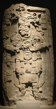 Una escultura en relieve con una figura humana lujosamente vestida mirando a la izquierda con las piernas ligeramente apartadas. Los brazos están doblados con las manos a la altura del pecho. Pequeñas columnas verticales de jeroglíficos se encuentran a cada lado de la cabeza, con otra columna abajo a la izquierda.