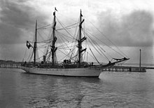 Photographie en noir et blanc d'un navire sortant d'un port.