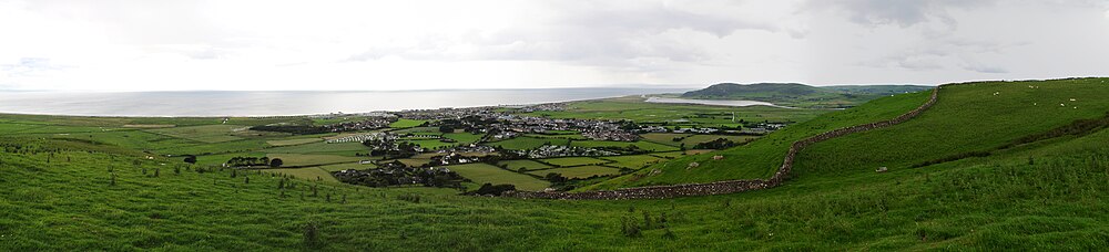 Panorama of the Welsh town Tywyn showing it nestled between hills and with the sea behind. A reservoir is visible in the background.