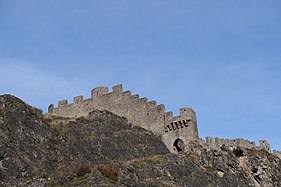 Crenellated stone wall following the contour of a rock.