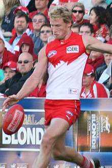 A blond-haired man kicks a red football