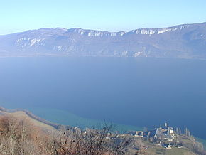 Photographie couleur montrant une abbaye située en bord de lac, faisant face à un massif montagneux situé de l'autre côté de l'eau.