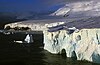 An ice front along a glaciated coast with a few rocks sticking out and a steep hill to the right