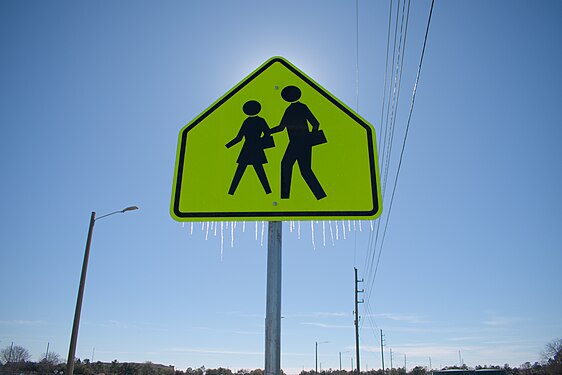 A pedestrian crossing sign with small icicles hanging off of it.