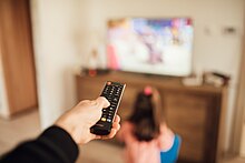 Parent using a remote control and young girl in front of a television in a blurry background