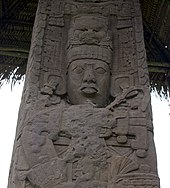 Close up of upper portion of an intricately carved stela, showing the face of a king with elaborate headdress and jewellery