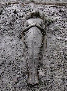 Headless stone statue of woman in draped cloth holding a sword