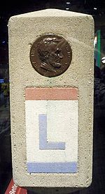 The Lincoln Highway was marked with small concrete obelisks. Towards the top of the marker was a profile of Abraham Lincoln. Below the profile, the route is marked with an L painted in red, white, and blue, the colors of the Lincoln Highway.