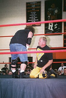 Deux catcheurs sont sur un ring. A gauche, Raven et à droite, Shane Douglas. Raven est debout, un peu penché vers l'avant. Douglas est à genou, regardant à gauche. Ils se font face. Raven porte un t-shirt noir, un short en jeans coupé et des rangers et Douglas porte un t-shirt noir avec ses initiales, un collant jaune et des bottes de catch.