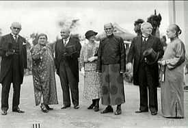 outdoor shot with four men and three women: three (Western men) wearing top hat and tails and one oriental-looking man wearing Chinese garments; two of the three women wearing Chinese robes, one wearing western dress with hat