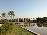 A pavilion built in a 1960s modern architecture style surrounded by Middle Eastern vegetation and a partially drained pool. The interior is decayed from a lack of maintenance.