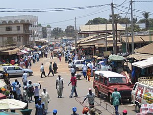 A street with several buildings on each side. Many pedestrians and some cars are on the street.