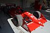 A red racing car adorned with sponsors logos and the number 11 in white on the front wing is primarily stationary in the shade and partially in sunlight