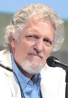 Portrait d'un homme âgé, aux cheveux et barbe blanches, souriant, en costume blanc.