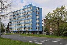 Blau-weißes Bürohochhaus mit Logo der Firma Telefunken, daneben ein noch älter Backsteinbau