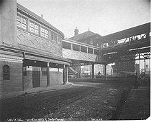 A two-story structure connected with a footbridge to an elevated rapid transit station