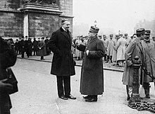 Photographie noir et blanc d'un homme en civil, grand, et d'un homme en uniforme militaire, plus petit, lui parlant.