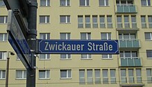 blaues Schild mit dem Straßennahmen vor einem Hochhaus