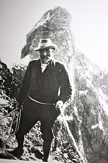 Photo en noir et blanc d'un homme tenant une corde avec une montagne en arrière-plan.