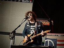 Ryan Adams tampil di depan mikrofon sambil memegang gitar.