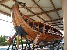 A galley sitting on struts on land under in an open-sided shed seen from the rear