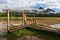 Banc suspendu et hamacs en osier sur une passerelle temporaire en bambou, dans les rizières devant des montagnes, un jour ensoleillé avec brume et ciel bleu, au restaurant Thongna Pha Puak (ທົ່ງນາຜາປວກວັງວຽງແດນງາມ), durant la mousson, à Vang Vieng.