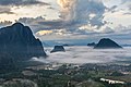 Pitons karstiques au lever du soleil, avec des nuages colorés au-dessus et une mer de nuages au-dessous, recouvrant les rizières inondées, vue sud depuis le sommet du mont Nam Xay, durant la mousson, à Vang Vieng.