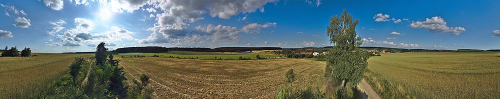 360° panorama Nivy, v pozadí lze sledovat rybník napájený Bílou vodou, nad ním spoza lesa trčí dvě turbíny protivanovských větrných elektráren, úplně vpravo lze za místní BTS vidět vrchol vysílače Kojál