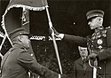 Commander of the Lithuanian Army Stasys Raštikis holds the Lithuanian Army flag with Vytis on obverse side, while a Lithuanian soldier swears his loyalty by kneeling in front of it