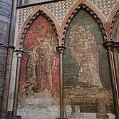 A wall with two paintings: one of two figures on a red background, and one of two figures on a green background