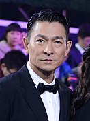 A serious-looking Andy Lau, seated and wearing a suit