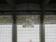 A tile mosaic on top of the outer wall of the Broadway Line platforms. The mosaic depicts the junction of Broadway and Bowery Road in 1828.