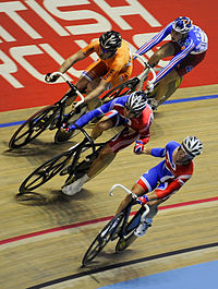 Cavendish passes a baton to Wiggins who is followed by two cyclists on the wooden track