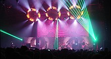 Musicians performing on stage in front of a crowd under many lights of different colors.